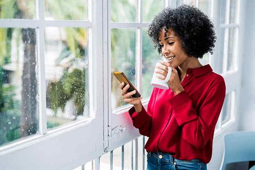woman-standing-near-window-looking-at-cell-phone woman-standing-near-window-looking-at-cell-phone